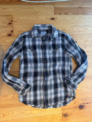 Rutig långärmad skjorta i bomull - Snygg rutig skjorta i svart, vit och grå med inslag av rött. Klassisk modell med krage, bröstfickor och knappar framtill. Tillverkad i mjuk bomull och perfekt för lager på lager. Passar dig som gillar en avslappnad men stilren look.