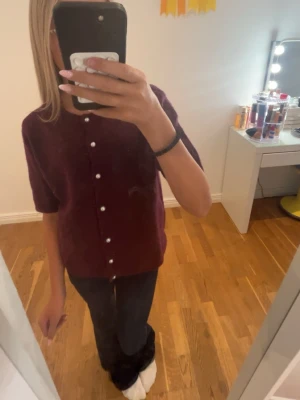 Vinröd kofta med pärlknappar 157 - Vinröd stickad kofta från 157 med kort ärm och pärlknappar framtill. Koftan har rund halsringning och är gjord i ett mjukt, luddigt material. Perfekt för lager-på-lager och en trendig look.