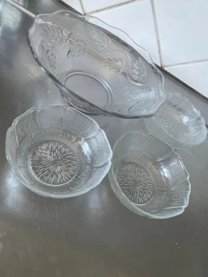 Set med glasskålar med blommönster - Säljer ett set med tre mindre glasskålar och en större serveringsskål. Alla skålar är genomskinliga med blommönster och bladdekor i glaset. Perfekt för servering av sallad, snacks eller dessert. Klassisk design som passar i alla kök.
