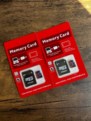 MicroSD-adapter med minneskort 2TB - Två paket med microSD-adapter och minneskort. Förpackningarna är röda och innehåller en svart microSD-adapter samt ett litet minneskort. Passar till laptop, smartphone och kamera. Perfekt för lagring och snabb dataöverföring. Två stycken 2TB utrymme varsin. 