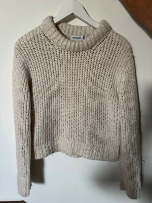 Beige stickad tröja från Weekday - Stickad tröja i beige från Weekday med grov ribbstickning och hög krage. Tröjan har långa ärmar och avslappnad passform, perfekt för kyliga dagar. Materialet ser mjukt och mysigt ut, och modellen är något kortare i midjan.