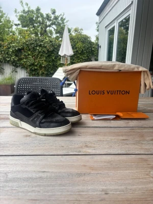 Louis Vuitton trainers - Snygga svarta Louis Vuitton sneakers med vita och ljusgröna detaljer på sulan. Skorna har klassisk låg profil, LV-logga på sidan och är tillverkade i en mix av mocka och läder. Perfekta för dig som vill ha en exklusiv och trendi