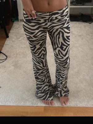 Zebramönstrade utsvängda leggings - Säljer ett par zebramönstrade leggings med svartvita ränder och utsvängda ben. De har hög midja och är stretchiga för en bekväm passform. 