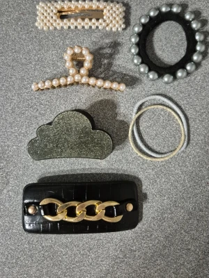 Mix av håraccessoarer med pärlor och glitter - Säljer ett set med sex håraccessoarer: två hårklämmor med pärlor, ett svart hårband med stora silverfärgade pärlor, ett glittrigt molnformat hårspänne, två elastiska hårsnoddar (en vit och en beige) samt ett svart hårspänne med guldfärgad kedjedetalj. Perfekt för att piffa upp frisyren.