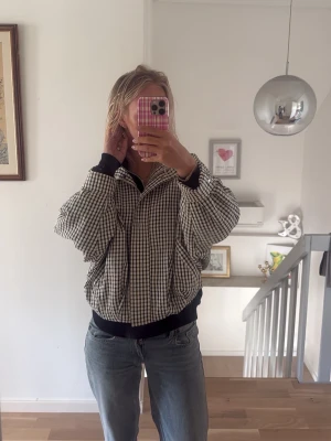 Rutig bomberjacka med dragkedja - Snygg rutig bomberjacka i svart och vitt med dragkedja framtill och bred krage. Jackan har en avslappnad passform och är tillverkad i ett mjukt tyg som ger en cool och trendig look. Använd 2 gånger. 