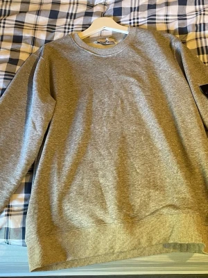 Grå basic sweatshirt - En enkel och stilren grå sweatshirt med rund hals och ribbade muddar vid ärmslut och nederkant. Perfekt för en avslappnad look och lätt att matcha med andra plagg. Tillverkad i mjukt material för extra komfort.