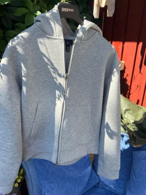 Grå zip hoodie från H&M - Snygg grå hoodie från H&M med dragkedja framtill och stor huva. Modellen är loose fit och har två stora fickor på magen. Tillverkad i mjukt sweatshirtmaterial som är perfekt för chill dagar. Enkel och stilren design som passar till det mesta.