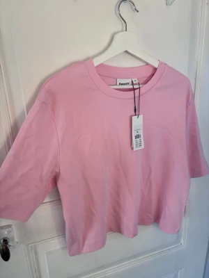 Ljusrosa t-shirt från Kappahl - En ljusrosa t-shirt från Kappahl i mjuk bomull. Modellen har korta ärmar, rund halsringning och en relaxed passform som ger en chill vibe. Perfekt att matcha med jeans eller shorts för en enkel och snygg look.