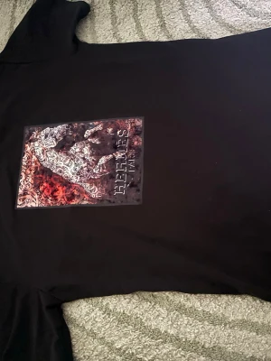 Svart t-shirt tryck - Cool svart t-shirt med stort färgstarkt tryck på bröstet. Trycket föreställer en häst i vitt och rött med detaljerat mönster. Perfekt för dig som vill sticka ut med en unik design.