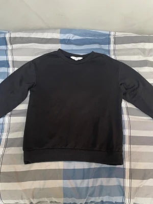 Svart basic sweatshirt - En enkel svart sweatshirt med rund hals och långa ärmar. Tröjan har en klassisk passform och ribbade muddar vid ärmslut och nederkant. Perfekt för en avslappnad stil och lätt att matcha med andra plagg.