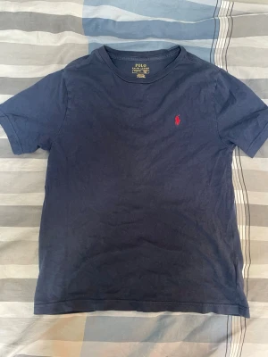 Marinblå t-shirt från Polo Ralph Lauren - Klassisk marinblå t-shirt från Polo Ralph Lauren med rund hals och korta ärmar. Liten röd logga broderad på bröstet. Perfekt basic-plagg som funkar till allt och är riktigt skön att bära.