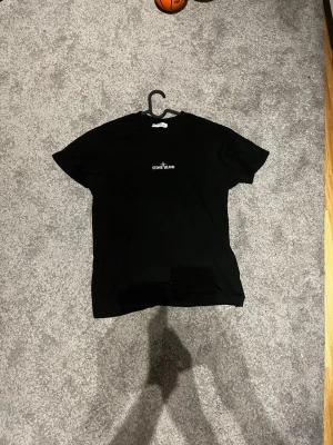 Svart Stone Island t-shirt - Säljer en svart t-shirt från Stone Island med logga tryckt på bröstet och stort grafiskt tryck med text och kompass på ryggen. Klassisk passform och korta ärmar, perfekt till streetwear-stilen.