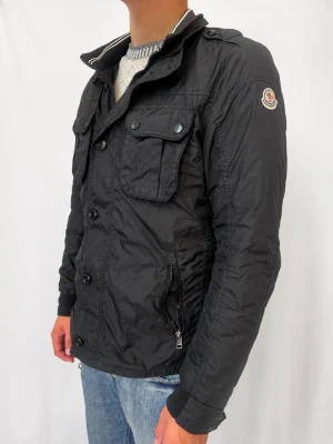 Moncler Field Jacket - Tja, vi säljer nu en field jacket från Moncler, den är extremt fet och självklart äkta! Den är köpt på monclers egna hemsida för ett tag sen, så jag kan säkert hitta fram kvittot om ni vill! Jackan är i storlek 3 vilket passar M-L! Killen på bilden är 181 cm lång och har Medium, men jackan passar även L. Jackan är I nytt skick, använd ett par gånger ! Det finns inga defekter på jackan ser helt ny ut! Därför kommer vi sätta priser 1599 kr! Priset är inte hugget I sten! Äktehets bevis i slutet!