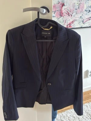 Mörkblå randig kavaj från STOCKH LM - Snygg mörkblå kavaj med diskreta vita ränder från STOCKH LM. Klassisk modell med smal passform, en knapp framtill och två fickor. Perfekt för en stilren look. Materialet är slätt och fodrat för extra komfort.
