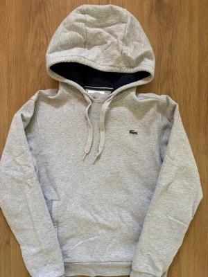 Lacoste Hoodie - Snygg grå Lacoste hoodie med snören. Skicket är mycket bra. Storleken är XS. Skriv om ni har några funderingar.