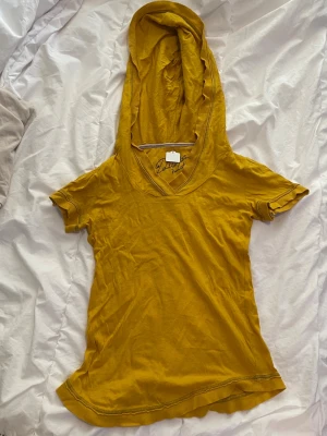 Gul hoodie med kort ärm och huva - Snygg gul hoodie med korta ärmar och stor huva. Tröjan har en djup v-ringning och är köpt second hand i Japan 