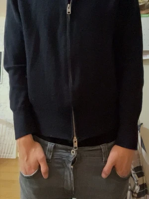 Svart ziptröja med hög krage - Snygg svart ziptröja med hög krage och hel dragkedja framtill. Tröjan har långa ärmar och en minimalistisk design som passar till det mesta. Perfekt för dig som gillar en clean och stilren look.