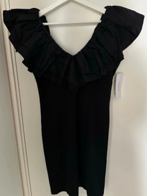 Bubbleroom Flounce Short Dress – ny med prislapp - Modell: Flounce Short Dress.  Helt ny svart klänning från Bubbleroom i storlek M med prislapp kvar. Figurnära modell med elegant volangdetalj och dragkedja baktill. Aldrig använd. Passar perfekt till middag, fest, bröllop eller andra finare tillfällen.