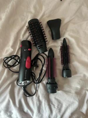 Remington varmluftsborste med tillbehör - Säljer en svart och rosa varmluftsborste från Remington med flera utbytbara borsthuvuden och stylingmunstycke. Perfekt för att skapa volym, lockar eller släta frisyrer. Passar dig som vill fixa håret snabbt och enkelt hemma. Använd endast en gång, precis som ny, inget hår på den.