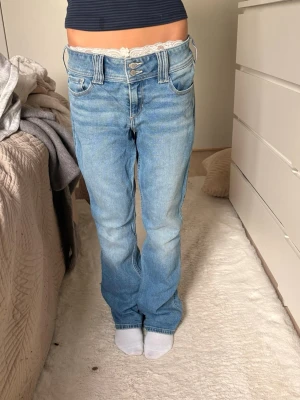 Ljusblå bootcut jeans med broderi - Säljer ett par ljusblå bootcut jeans med dubbla knappar och broderade detaljer på bakfickorna. Jeansen har låg midja och klassisk femficksmodell. Materialet är denim i bomull och passformen är avslappnad med lätt utsvängda ben.