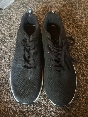 Svarta sneakers med vit sula - Snygga svarta sneakers med ovandel i mesh-tyg och klassisk snörning. Skorna har en vit sula med svart mönstrad undersida för bra grepp. Perfekta för en sportig och avslappnad stil.