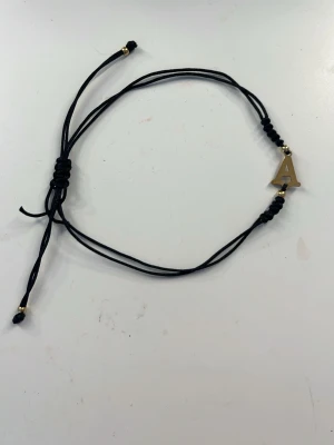 Svart armband med bokstav A - Snyggt svart armband med justerbar knytning och en guldfärgad bokstav A som detalj. 