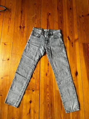 Grå tvättade raka jeans 29/32 - Säljer ett par grå tvättade jeans med rak passform och klassisk femficksdesign. Jeansen har normal midja och bälteshällor, samt snygga kontrastsömmar. Perfekta för en avslappnad och trendig look.