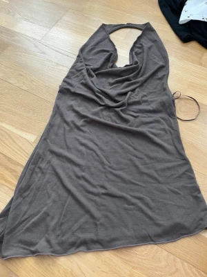 Brun halterneckklänning från Nelly - Säljer en brun halterneckklänning från Nelly i mjukt, stretchigt material. Klänningen har en snygg draperad front och är ärmlös med öppen rygg. Perfekt för dig som gillar en enkel men trendig look.