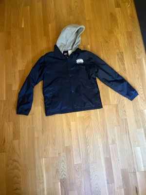 Svart vindjacka med grå luva Vans - Snygg svart vindjacka från Vans. Äkta! Saknar en knapp längst upp’