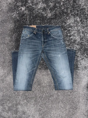 Blå slitna jeans med tvättade detaljer från Dondup - Säljer ett par blå jeans med snygga slitningar och tvättade detaljer. Jeansen har fem fickor, raka ben och kontrastsömmar. Perfekta för en avslappnad och trendig look.