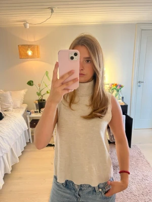 Beige ärmlös polotopp - Säljer en beige ärmlös polotopp i mjukt stickat material. Toppen har hög ribbad krage och en loose passform. Köpt begagnad men väldigt bra skick!💗