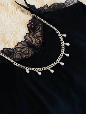 Silverfärgat halsband med pärldroppar - Säljer ett snyggt halsband i silverfärg med rostfritt kedja och droppformade pärlor som hänger längs hela halsbandet. Perfekt för dig som vill ha en unik accessoar som sticker ut. 