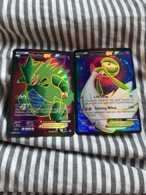 Pokémon EX samlarkort Tyranitar & Gardevoir - Två Pokémon EX samlarkort: Tyranitar EX och Gardevoir EX. Korten har holografisk yta och färgstarka illustrationer i grönt, blått och regnbågsfärger. Perfekt för dig som gillar Pokémon, samlar på kort eller vill ha något unikt till din samling.