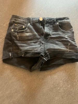 Svarta jeansshorts från FB Sister - Säljer ett par svarta jeansshorts från FB Sister i storlek S. Shortsen har slitna detaljer, fem fickor och uppvikta benslut. Perfekta för dig som gillar en avslappnad och trendig stil.