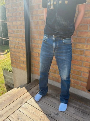 Blå raka jeans med slitningar - Säljer ett par klassiska blå jeans med raka ben och lätt slitna detaljer framtill. Jeansen har fem fickor och normal midja. Perfekta för en avslappnad och stilren look. Materialet är denim i bomull.