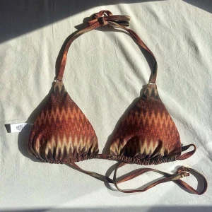 Glittrig mönstrad bikini  - Superfin triangelformad bikinitopp i brunt/bronsigt missoni-inspirerat mönster. Glittrar superfint och har gulddetaljer. Modellen ”Golden Chevron”  Storlek S/36 och helt ny med lappar kvar. Köpt för 419kr och glömde lämna tillbaka i tid❤️🤎