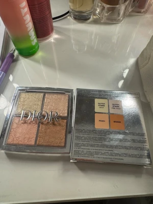 Dior Backstage Glow Face Palette - Glow Face Palette från Dior med fyra highlighters i nyanserna glitter gold, glitter pink gold, peach och bronze. Paletten har en lyxig silverfärgad förpackning och varje färg har en skimrig finish som ger glow till ansiktet. Perfekt för att framhäva kindben och ge lyster.