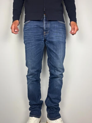 Nudie Jeans Co Dude Dan W33 L34 - Blåa Jeans Denim - Snygga Nudie Jeans i modellen Dude Dan med Dark Deep Worn tvätt. Mycket fint skick, A-B Grade Storlek W33 L34 i 99% bomull & 1% elastan. Mått [platt]: A: 43 cm B: 113 cm C: 27 cm D: 20 cm Passar bra på mig i bilden som är 189 cm lång men passar även längre. Skickas snabbt!