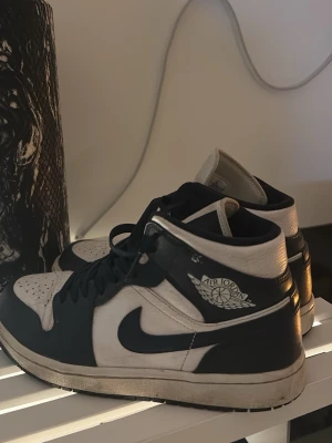Nike Air Jordan 1 mörkblå/vit - Snygga Nike Air Jordan 1 sneakers i mörkblå  och vitt läder med klassisk hög siluett och ikonisk Swoosh på sidan. Skorna har Air Jordan-logga på ankeln och robust gummisula med bra grepp. Perfekta för dig som gillar streetwear och vill sticka ut.