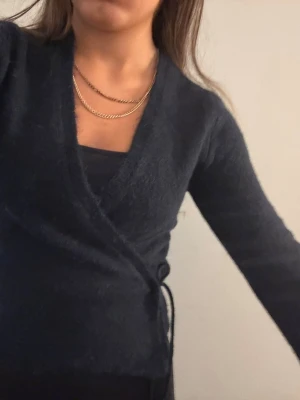 Mörkblå omlottkofta i fluffigt material - Snygg mörkblå omlottkofta med knytband i sidan. Koftan är gjord i ett mjukt och fluffigt material och har långa ärmar samt djup v-ringning. Perfekt för lager på lager och ger en trendig look.