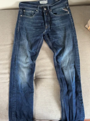 Mörkblå raka jeans med slitningar - Säljer ett par mörkblå jeans med raka ben och snygga slitningar framtill. Jeansen har klassiska fem fickor och kontrastsömmar på bakfickorna. Materialet är denim i bomull och passformen är avslappnad men ändå stilren.