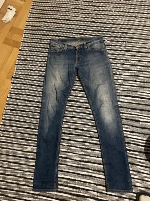Nudie slim fit jeans - Nudie jeans Snygga blå slim fit jeans med klassisk femficksdesign och slitna detaljer på låren. Jeansen har en medelhög midja och dekorativa sömmar på bakfickorna. Perfekta för en avslappnad och trendig look.