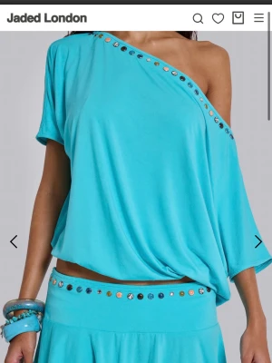 Turkos oneshoulder topp med nitar - Säljer en turkos oneshoulder topp från Jaded London. Toppen har en lös passform och är dekorerad med silverfärgade nitar längs den asymmetriska halsringningen. Perfekt för dig som vill sticka ut med en färgstark och unik stil.