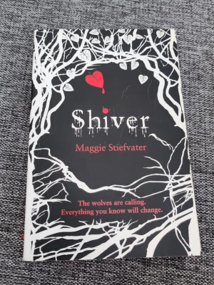 Shiver av Maggie Stiefvater - En ungdomsroman med svart och vit omslagsdesign, dekorerad med vita trädgrenar och röda detaljer. Titeln 'Shiver' och författaren Maggie Stiefvater syns tydligt på framsidan. Perfekt för dig som gillar fantasy och romantik.