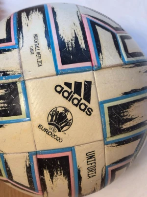 Adidas Uniforia fotboll Euro 2020 - Säljer en Adidas Uniforia fotboll, officiell matchboll-replika från UEFA Euro 2020. Bollen är vit med svart, blå, rosa och limegröna detaljer i ett grafiskt mönster. Perfekt för träning eller match på alla underlag.