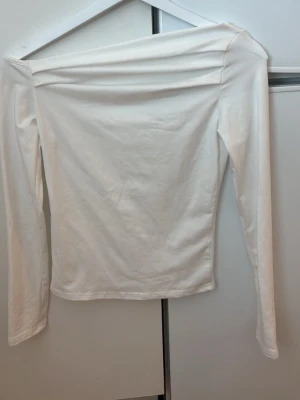 Vit offshoulder långärmad topp - Säljer en stilren vit offshoulder topp med långa ärmar. Toppen är i mjukt bomullstyg och har en enkel, clean look som passar till det mesta. Perfekt för dig som gillar minimalistisk stil.
