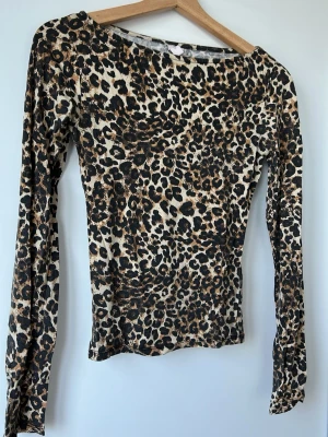 Leopardmönstrad långärmad topp - Snygg långärmad topp med leopardmönster i beige, svart och bruna toner. Figurnära passform och rund halsringning. Perfekt för dig som vill sticka ut med ett djurmönstrat plagg.