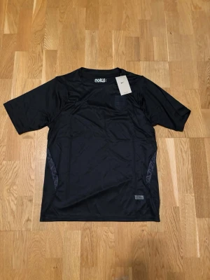 Svart Norge Nike t-shirt i funktionsmaterial - Snygg svart Norge t-shirt från Nike i funktionsmaterial, perfekt för dig som gillar sportig stil. T-shirten har korta ärmar, rund halsringning och diskret Nike-logga på bröstet. Enkel och stilren design som passar till det mesta.