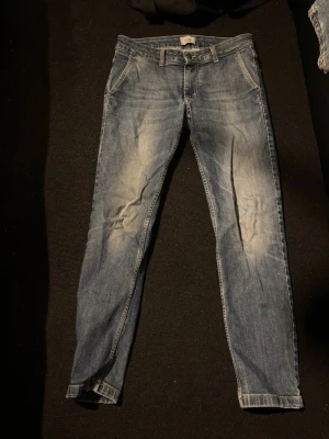 Blå slim fit jeans med slitningar - Snygga blå slim fit jeans med ljusa slitningar framtill och bakfickor. Klassisk femficksmodell med dragkedja och knapp. Jeansen har en tvättad look och raka ben, perfekta till en avslappnad stil. Köpta på libero milano i Milano 