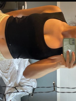 Svart croppad linnetopp  - Snygg svart croppad linnetopp med en stor cut-out detalj framtill. Toppen är ärmlös och har en tight passform som framhäver figuren. Perfekt för dig som vill ha en trendig och edgy look.